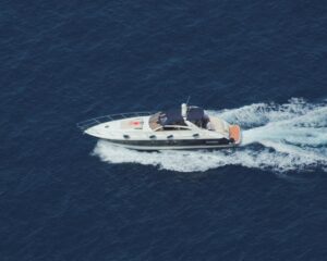Top-down view of a white motor yacht cruising through deep blue open water with a wake behind it.